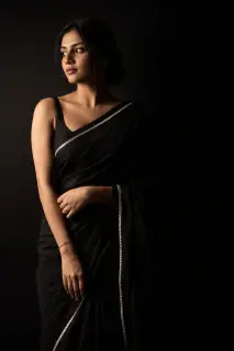 Woman in a black saree lit by a single hard light against a dark background