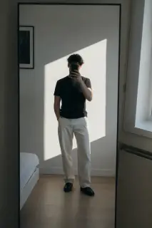Full-length mirror photograph with hard geometric sunlight across the wall